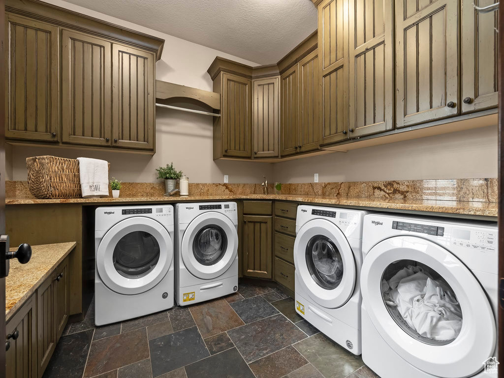 Washroom with cabinets, washing machine and dryer, a textured ceiling, and dark tile flooring