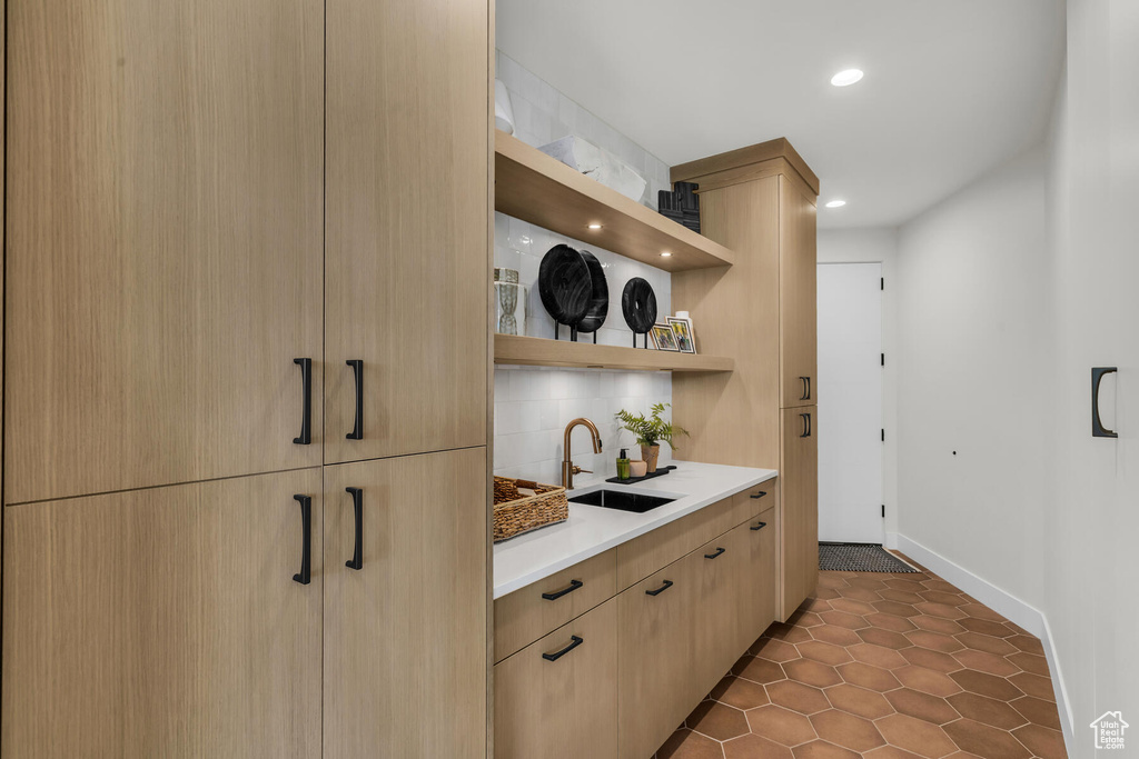 Kitchen with light brown cabinetry, tasteful backsplash, tile floors, and sink