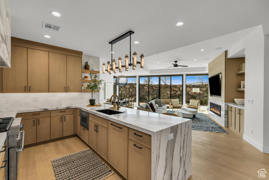 Kitchen featuring light stone countertops, ceiling fan, tasteful backsplash, light wood-type flooring, and sink