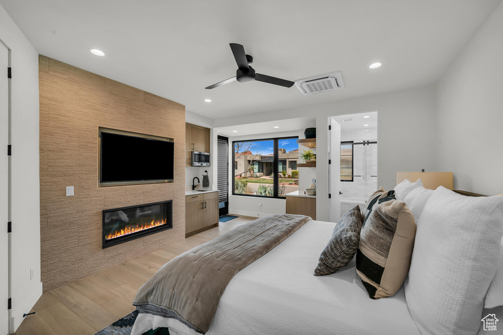 Bedroom featuring a large fireplace, connected bathroom, ceiling fan, and light hardwood / wood-style flooring