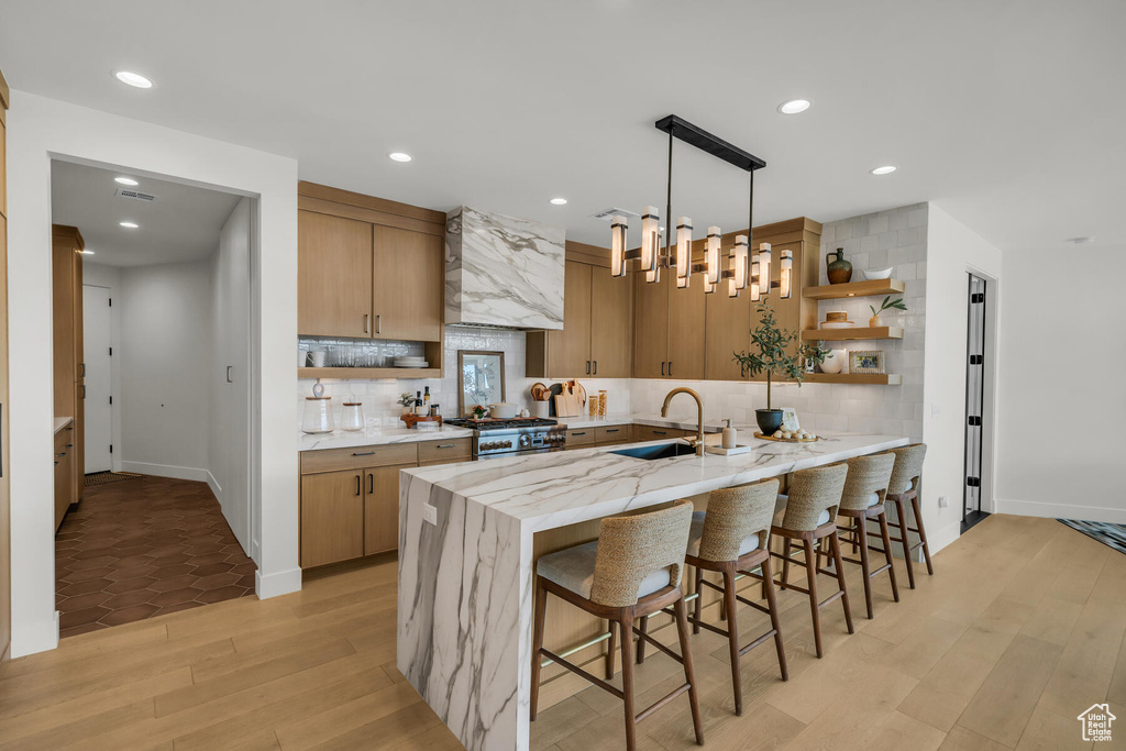 Kitchen with light stone countertops, decorative light fixtures, light hardwood / wood-style floors, sink, and tasteful backsplash