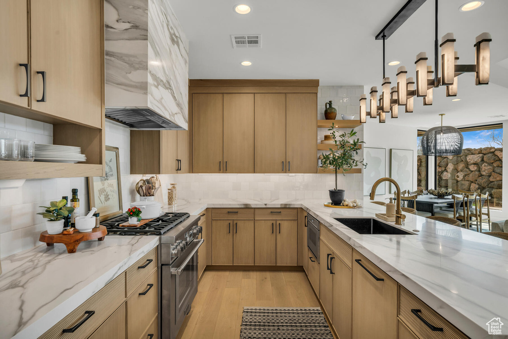 Kitchen with light stone countertops, backsplash, custom exhaust hood, light hardwood / wood-style flooring, and high end stove