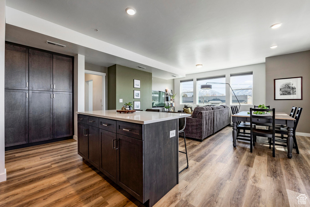 Kitchen featuring light hardwood / wood-style flooring, a kitchen island, dark brown cabinets, and a kitchen bar