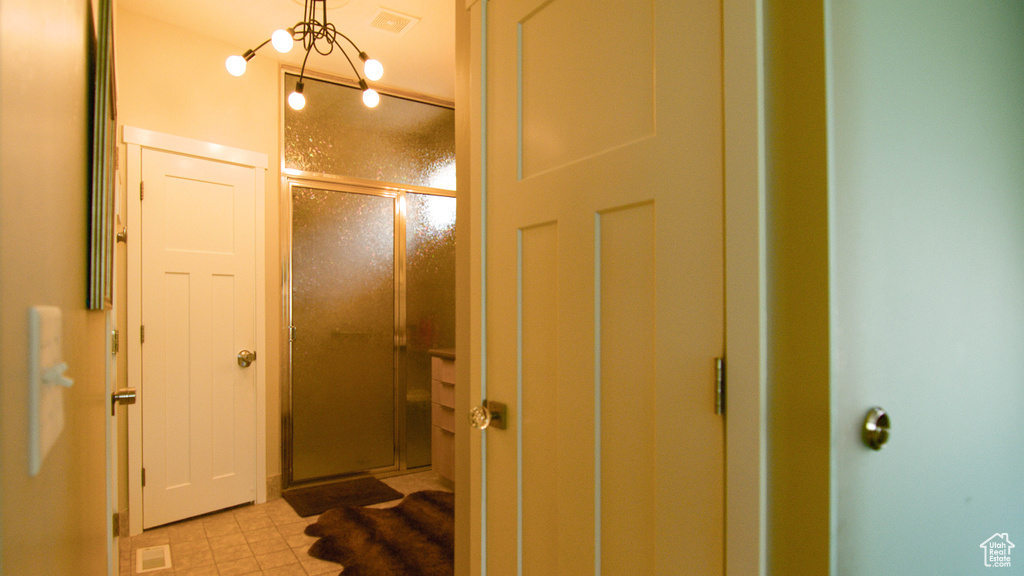 Bathroom with a notable chandelier, a shower with door, and tile floors