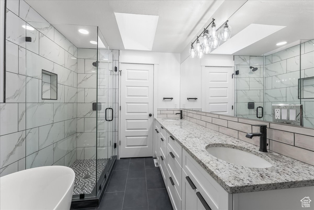 Bathroom featuring separate shower and tub, tile walls, a skylight, tile flooring, and dual bowl vanity
