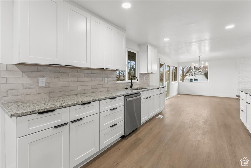 Kitchen with tasteful backsplash, light hardwood / wood-style flooring, dishwasher, an inviting chandelier, and white cabinets