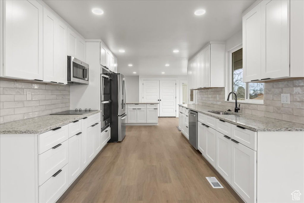 Kitchen with white cabinetry, light hardwood / wood-style flooring, tasteful backsplash, and stainless steel appliances