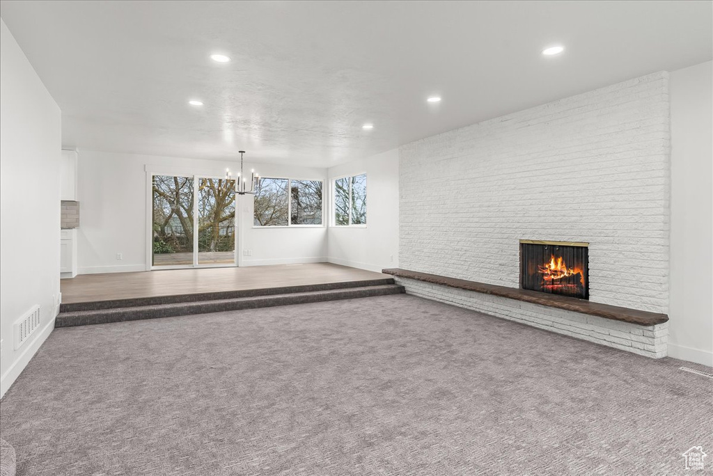 Unfurnished living room with carpet flooring, brick wall, a notable chandelier, and a fireplace