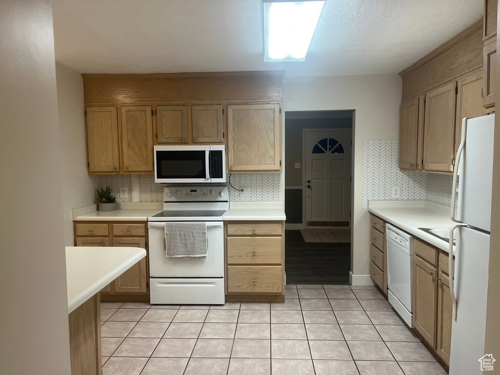 Kitchen with light tile floors, white appliances, tasteful backsplash, and light brown cabinetry