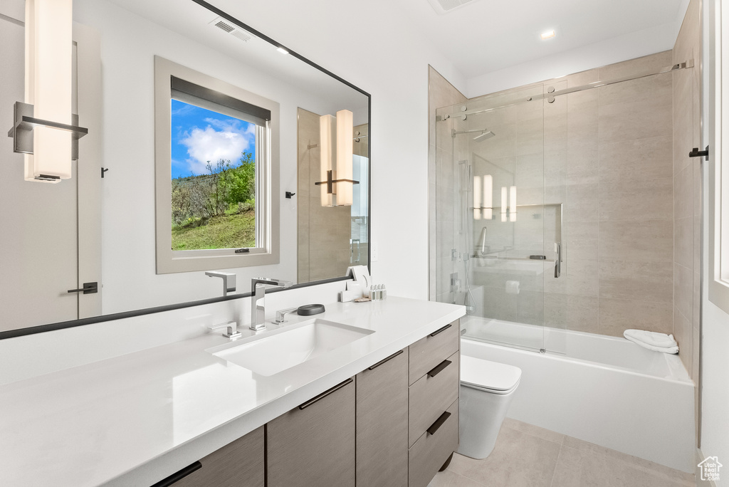 Full bathroom with tile floors, toilet, vanity, and shower / bath combination with glass door