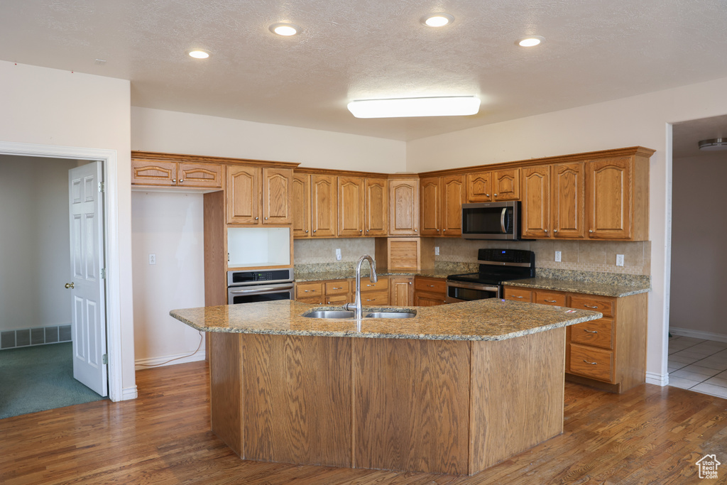 Kitchen featuring backsplash, stainless steel appliances, sink, an island with sink, and light stone countertops