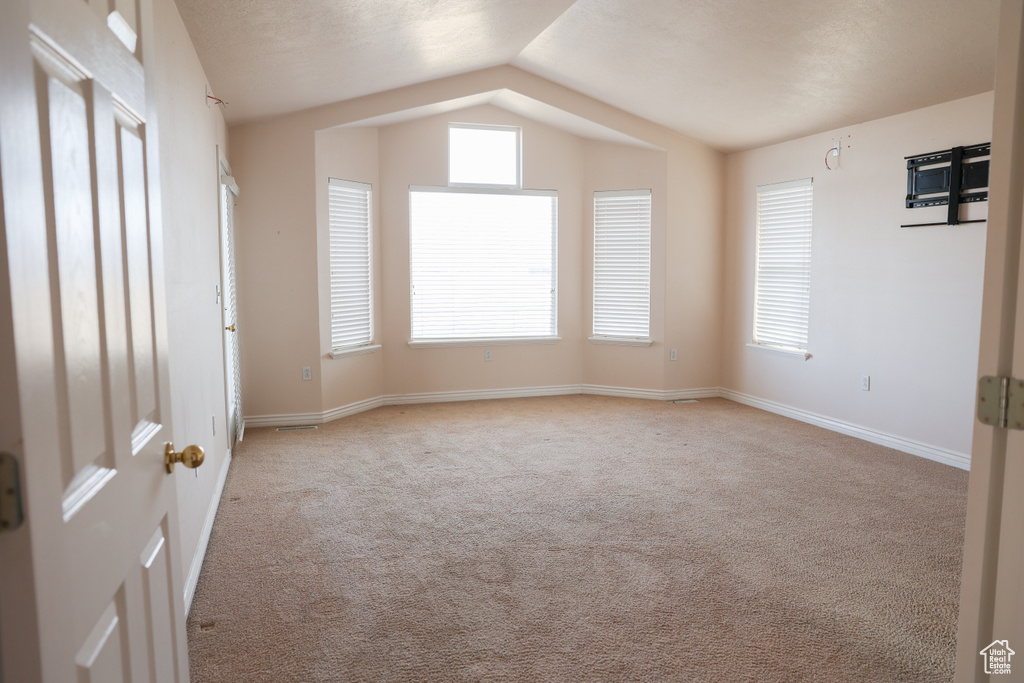 Carpeted spare room featuring vaulted ceiling