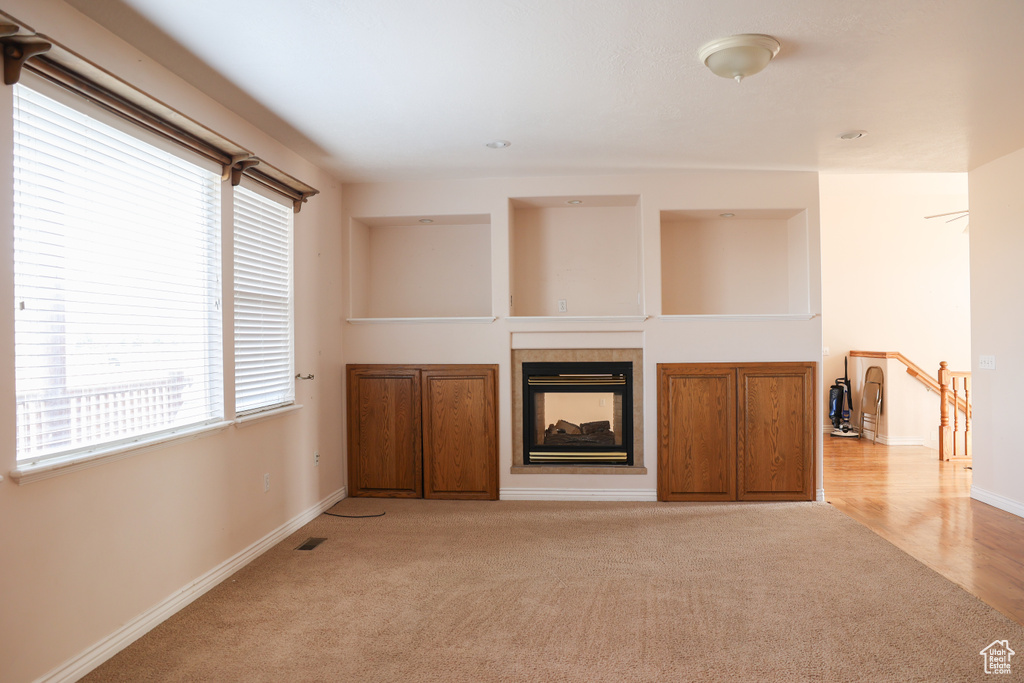 Unfurnished living room featuring a wealth of natural light, light carpet, and a fireplace