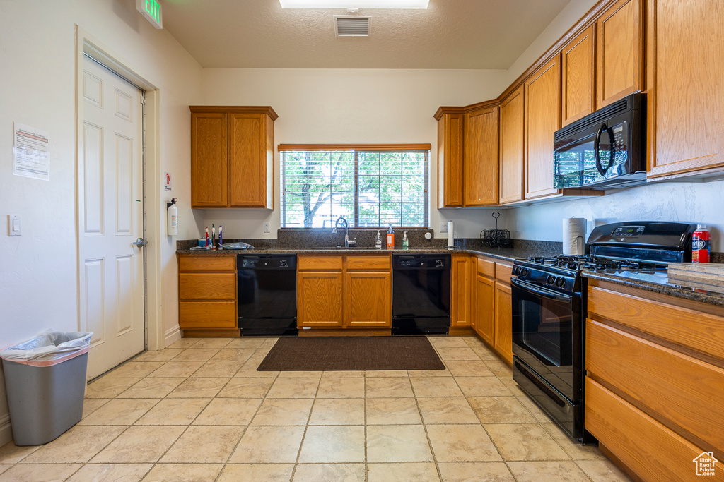 Kitchen featuring light tile flooring, sink, dark stone countertops, and black appliances