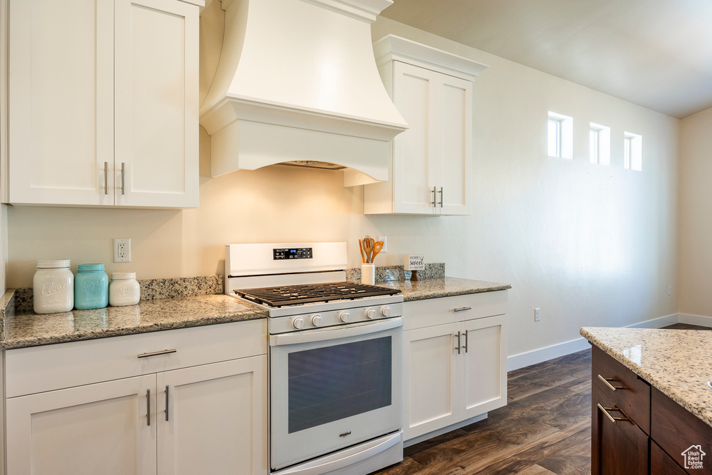 Kitchen featuring white range with gas stovetop, custom range hood, dark hardwood / wood-style floors, light stone countertops, and white cabinets