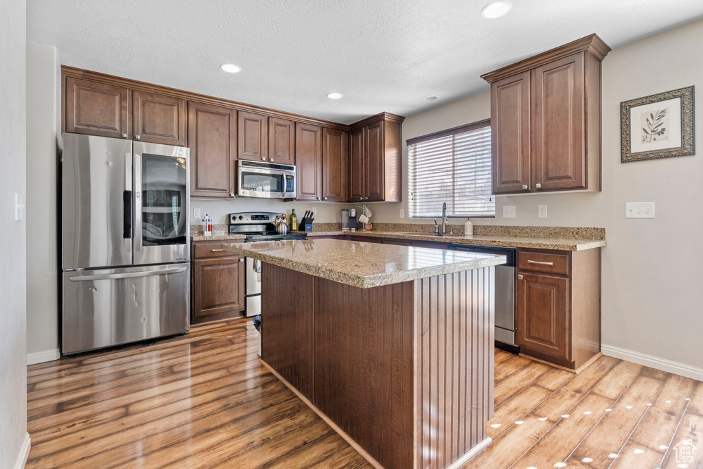 Kitchen featuring a center island, sink, appliances with stainless steel finishes, light hardwood / wood-style flooring, and light stone counters