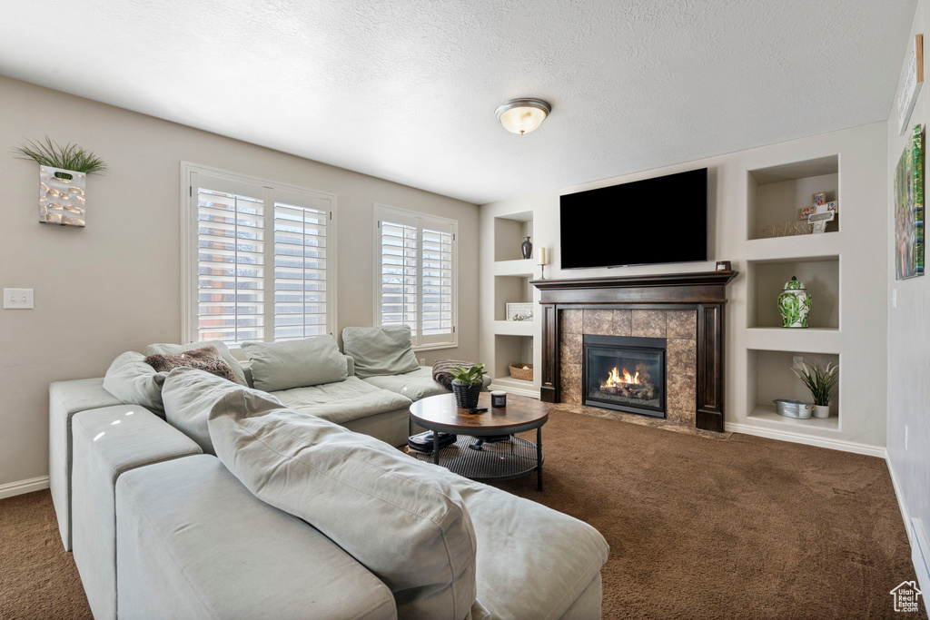 Living room featuring built in shelves, a tiled fireplace, a textured ceiling, and dark colored carpet