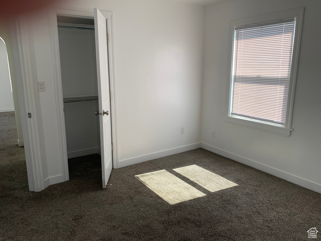 Unfurnished bedroom with dark carpet, multiple windows, a closet, and a spacious closet