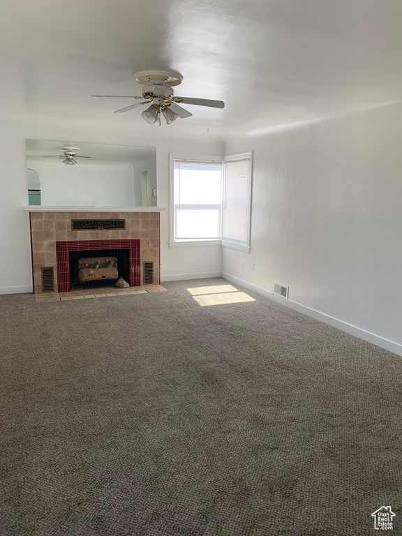 Unfurnished living room featuring carpet floors, ceiling fan, and a tile fireplace