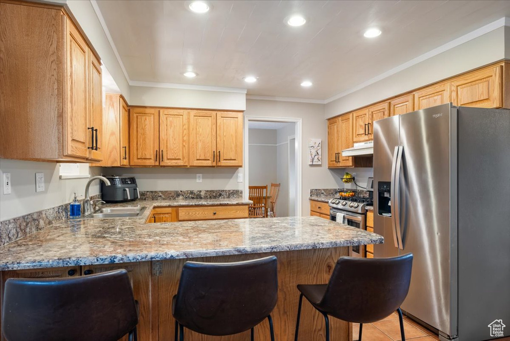 Kitchen with appliances with stainless steel finishes, ornamental molding, light stone counters, sink, and a breakfast bar