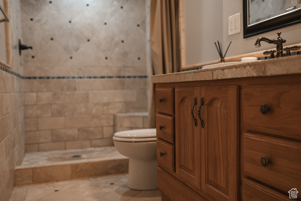 Bathroom featuring tiled shower, vanity, toilet, and tile floors