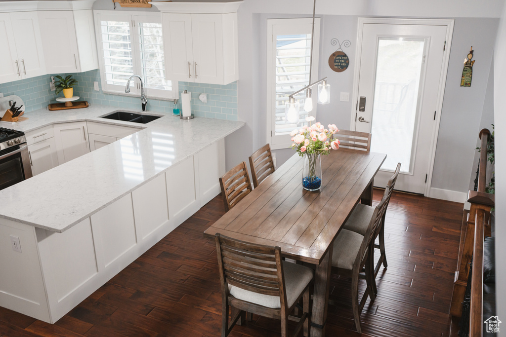 Kitchen with sink, white cabinets, hanging light fixtures, backsplash, and dark wood-type flooring