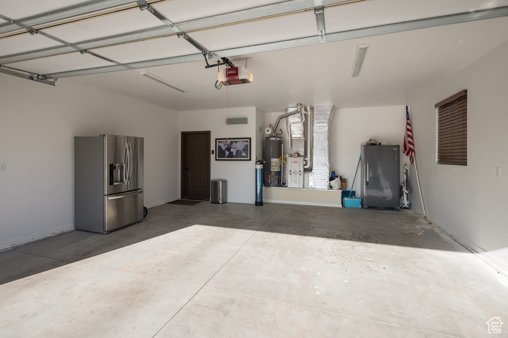 Garage with heating utilities, stainless steel fridge, refrigerator, water heater, and a garage door opener