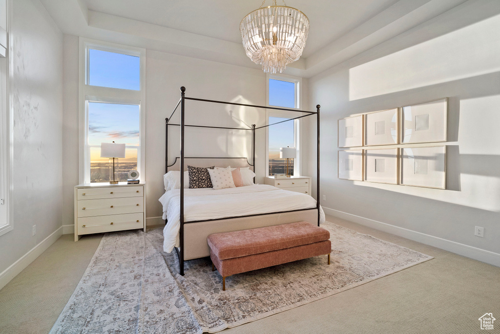 Bedroom with an inviting chandelier, light colored carpet, a tray ceiling, and multiple windows
