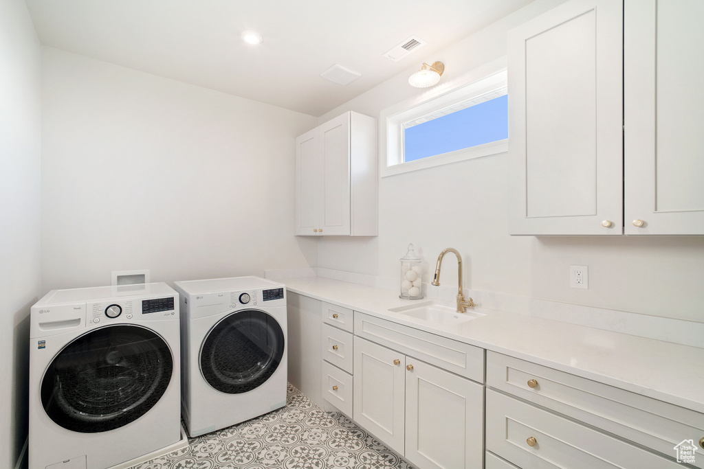 Washroom with light tile flooring, cabinets, sink, and washing machine and clothes dryer