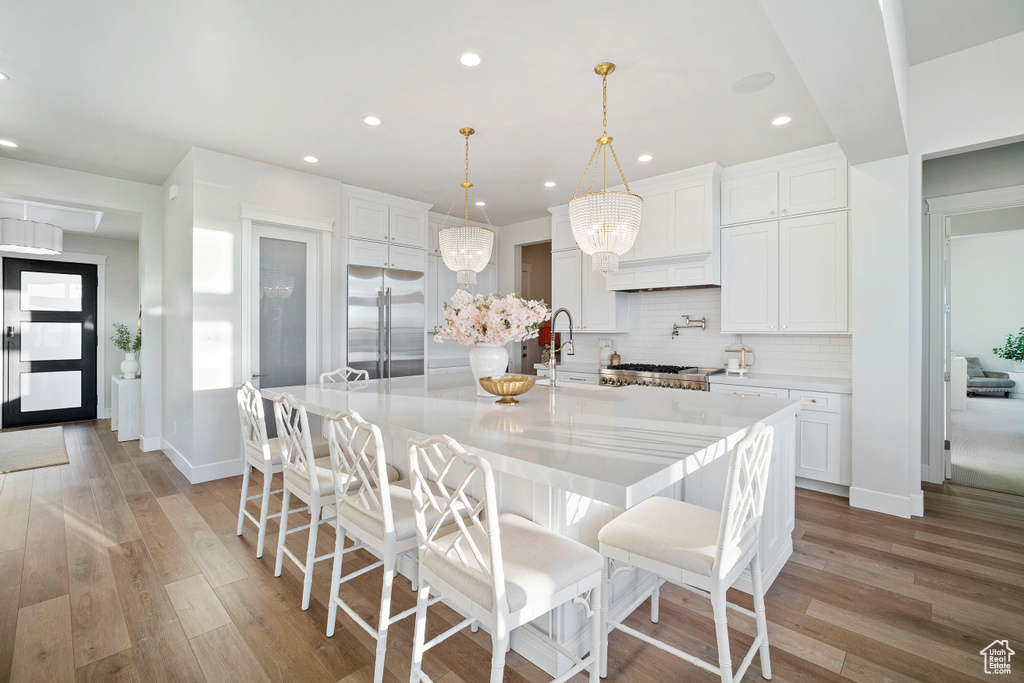 Kitchen with white cabinetry, light hardwood / wood-style floors, a kitchen island with sink, and high end fridge