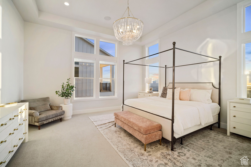 Carpeted bedroom featuring multiple windows, a chandelier, and a tray ceiling