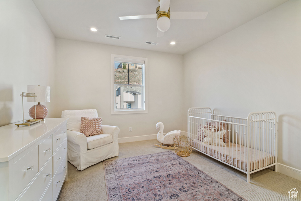 Bedroom featuring a nursery area, light carpet, and ceiling fan