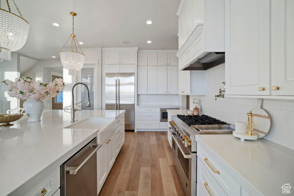 Kitchen featuring backsplash, white cabinets, light wood-type flooring, hanging light fixtures, and high end appliances