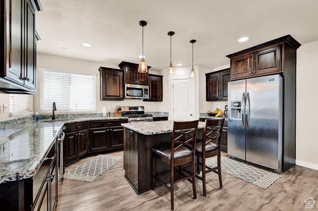 Kitchen featuring decorative light fixtures, a center island, light hardwood / wood-style floors, light stone counters, and stainless steel appliances