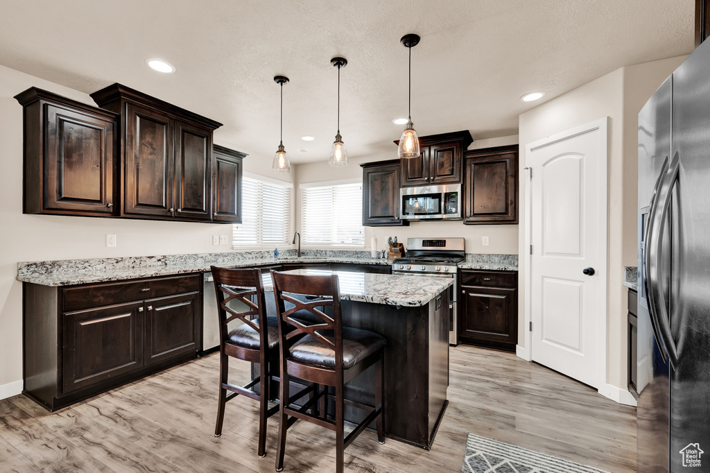 Kitchen with decorative light fixtures, a kitchen island, light hardwood / wood-style flooring, stainless steel appliances, and dark brown cabinets