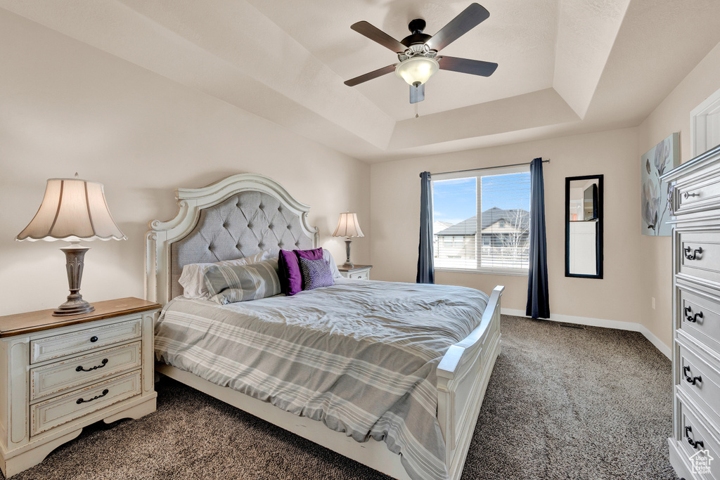 Bedroom with dark carpet, ceiling fan, and a raised ceiling