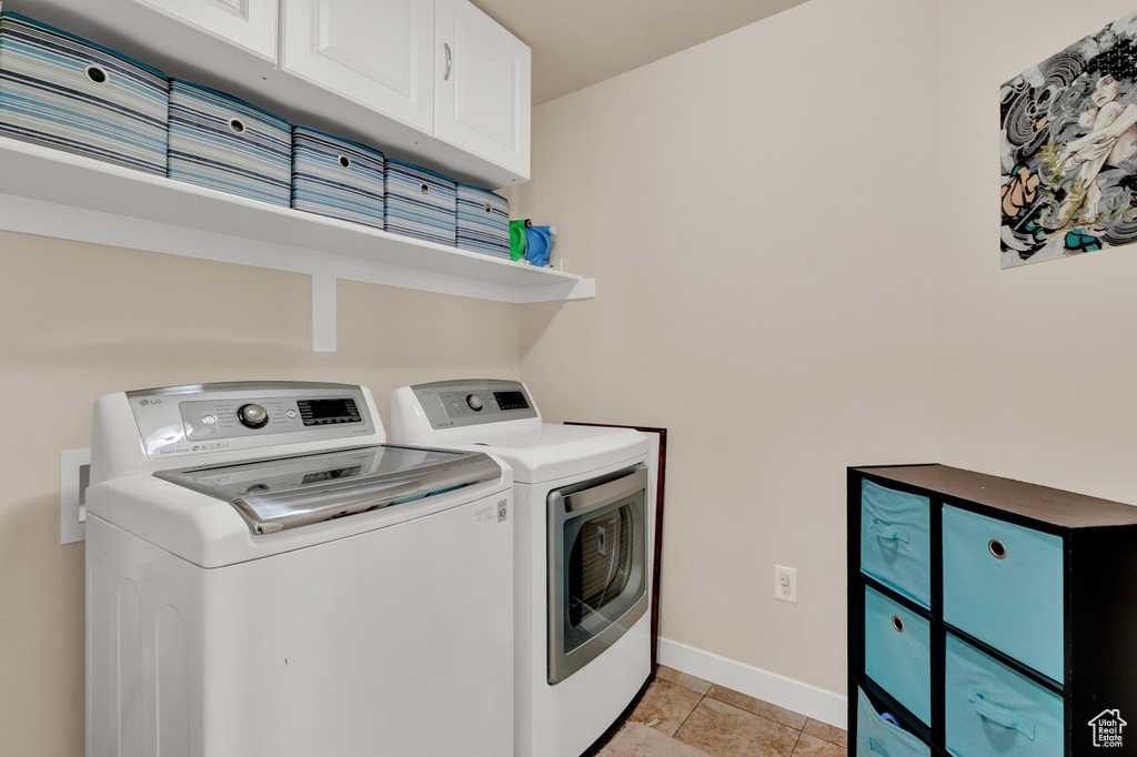 Clothes washing area with light tile floors, cabinets, and washing machine and clothes dryer