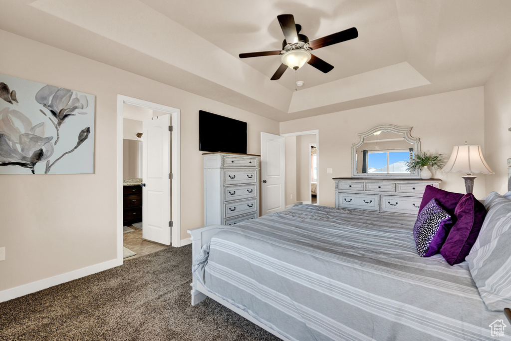 Carpeted bedroom featuring ensuite bath, a tray ceiling, and ceiling fan