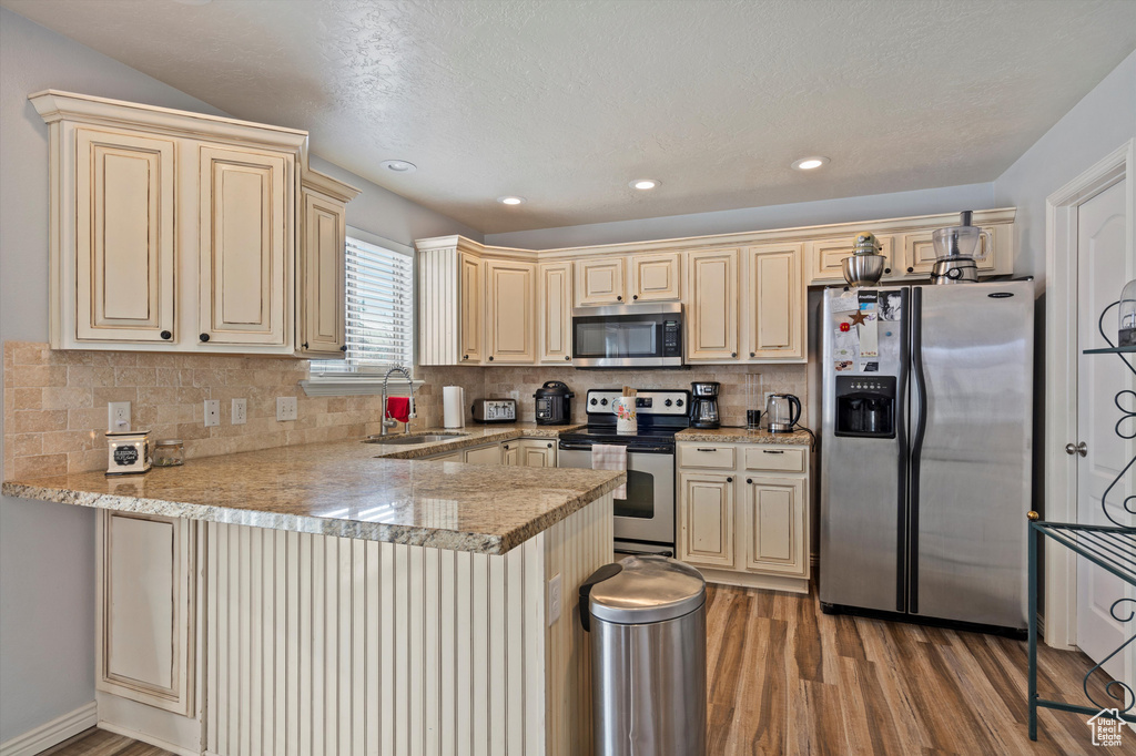 Kitchen with backsplash, stainless steel appliances, sink, and light hardwood / wood-style floors