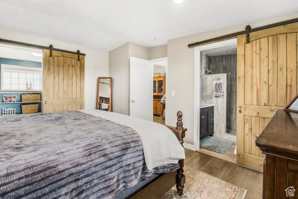 Bedroom featuring ensuite bathroom, a barn door, and dark wood-type flooring