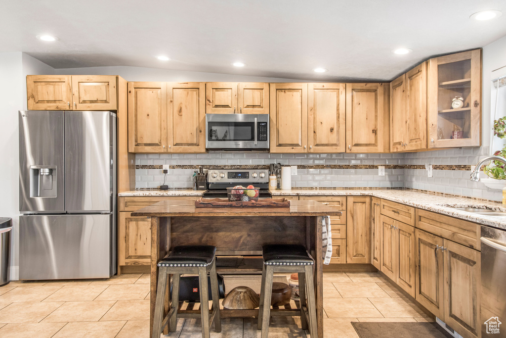 Kitchen featuring backsplash, light tile floors, stainless steel appliances, sink, and light stone countertops