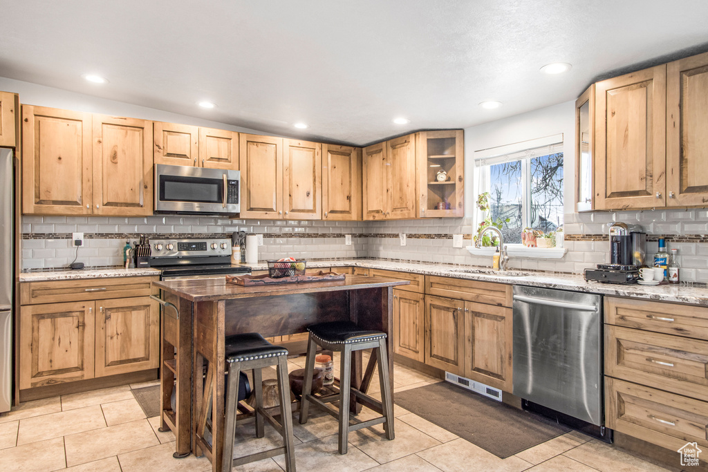 Kitchen with tasteful backsplash, light tile floors, stainless steel appliances, light stone counters, and sink