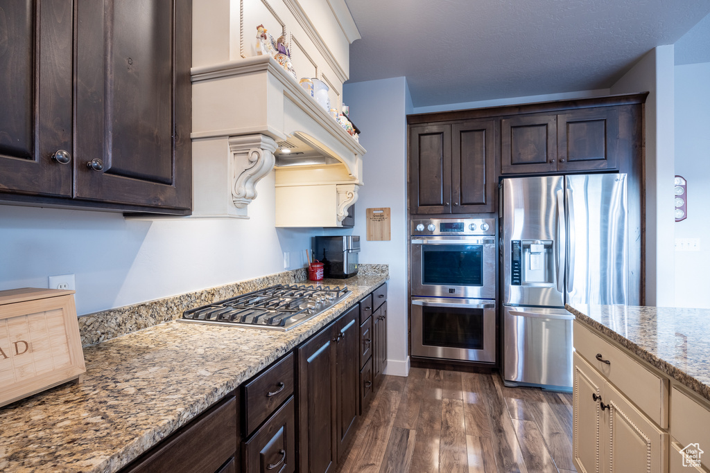 Kitchen featuring appliances with stainless steel finishes, dark brown cabinets, dark hardwood / wood-style flooring, and light stone counters