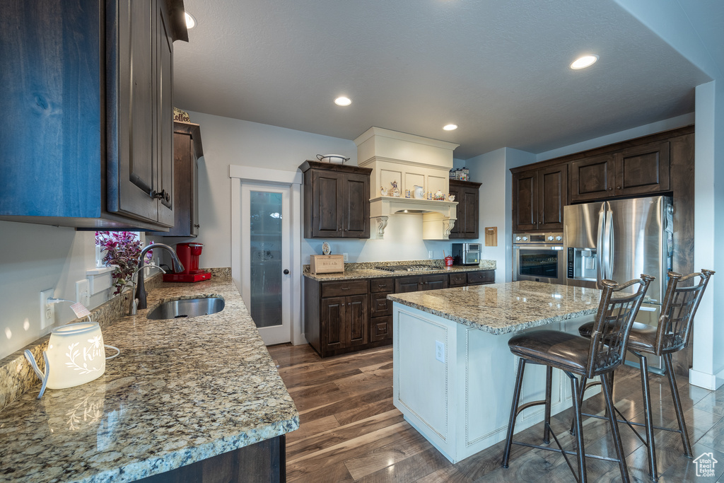 Kitchen featuring stainless steel appliances, sink, a breakfast bar area, dark hardwood / wood-style flooring, and light stone countertops