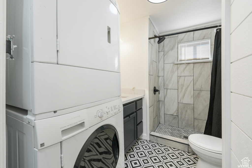 Bathroom with stacked washer and dryer, walk in shower, tile floors, vanity, and toilet