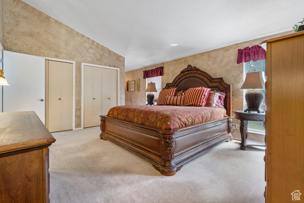 Bedroom with vaulted ceiling, light carpet, and multiple closets