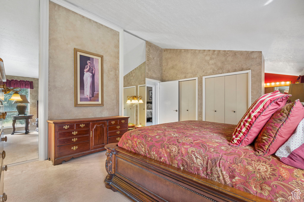 Carpeted bedroom with ensuite bathroom, two closets, a textured ceiling, and high vaulted ceiling