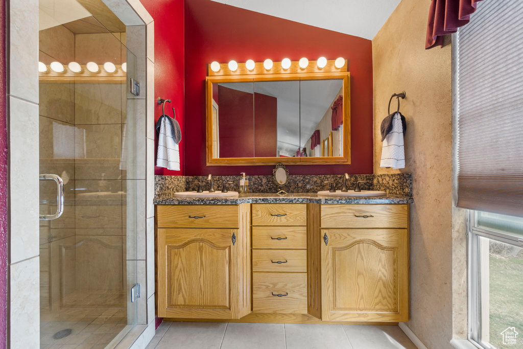 Bathroom featuring a shower with shower door, lofted ceiling, vanity with extensive cabinet space, and double sink
