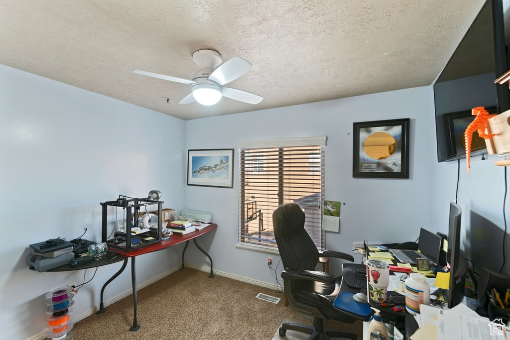 Office area featuring a textured ceiling, dark carpet, and ceiling fan