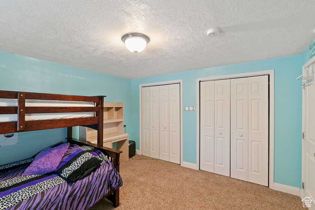 Bedroom with two closets, light carpet, and a textured ceiling